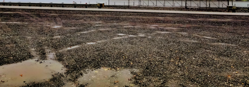 Standing water and rutted gravel on an industrial lot needing drainage correction
